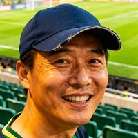 一位40岁左右的中国男性球迷头像，戴着棒球帽，背景是足球场看台，表情热情洋溢